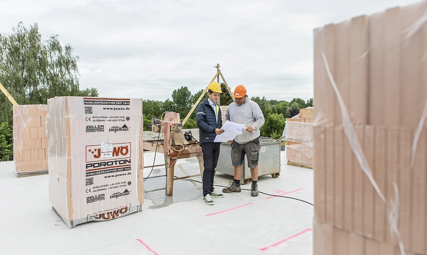 Bouwleider geeft uitleg aan een werkman op een werf terwijl ze samen de plannen bekijken.